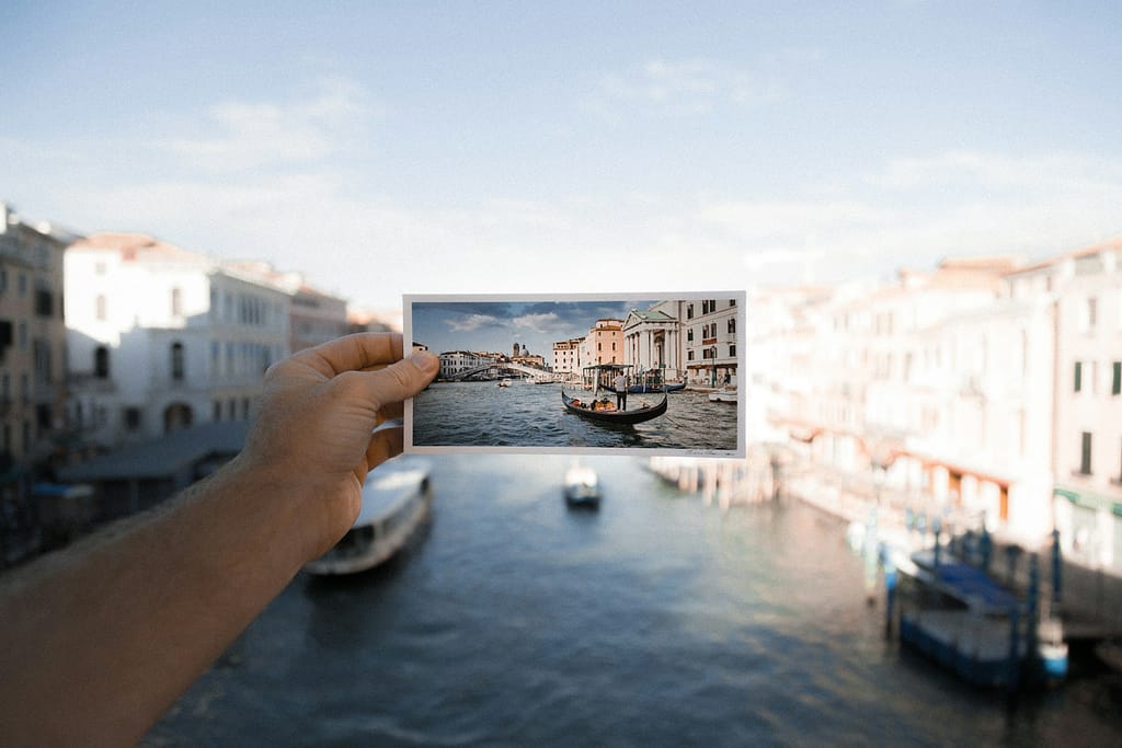 person holding photo of boat on body of water - souvenirs de voyages