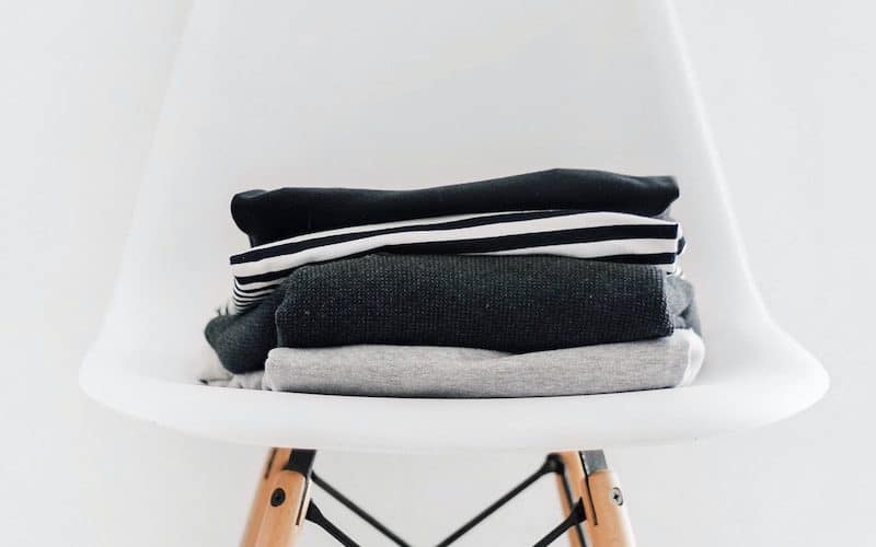pile of black, white, and gray textiles on white padded chair with brown frame