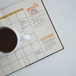 white ceramic mug with coffee on top of a planner